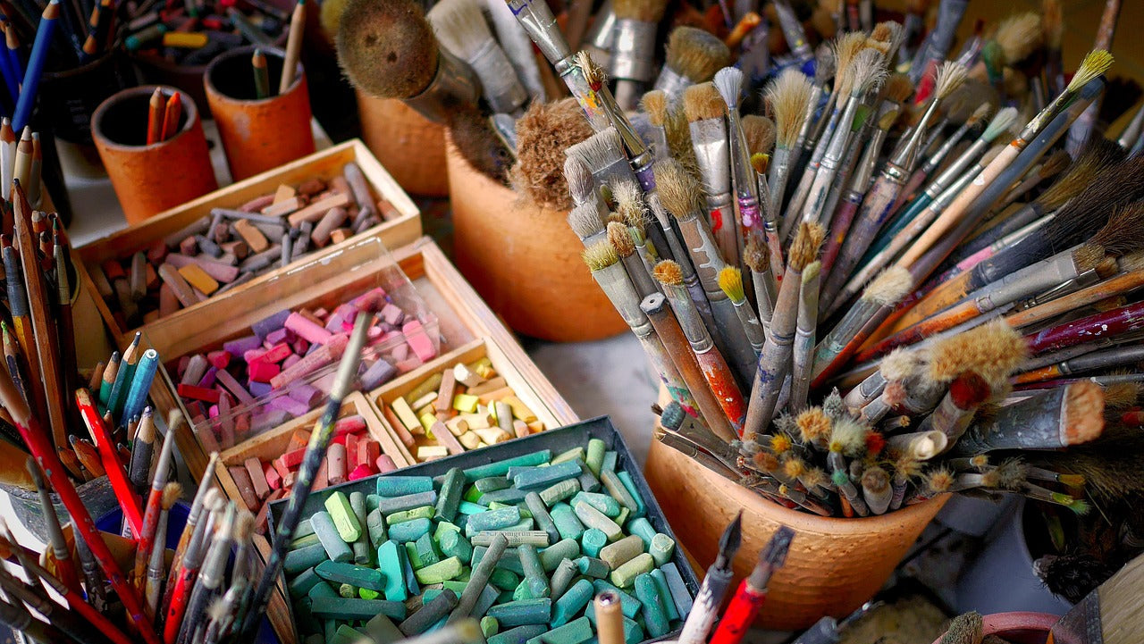 Collection of art supplies including brushes, pastels, and pencils on a table.