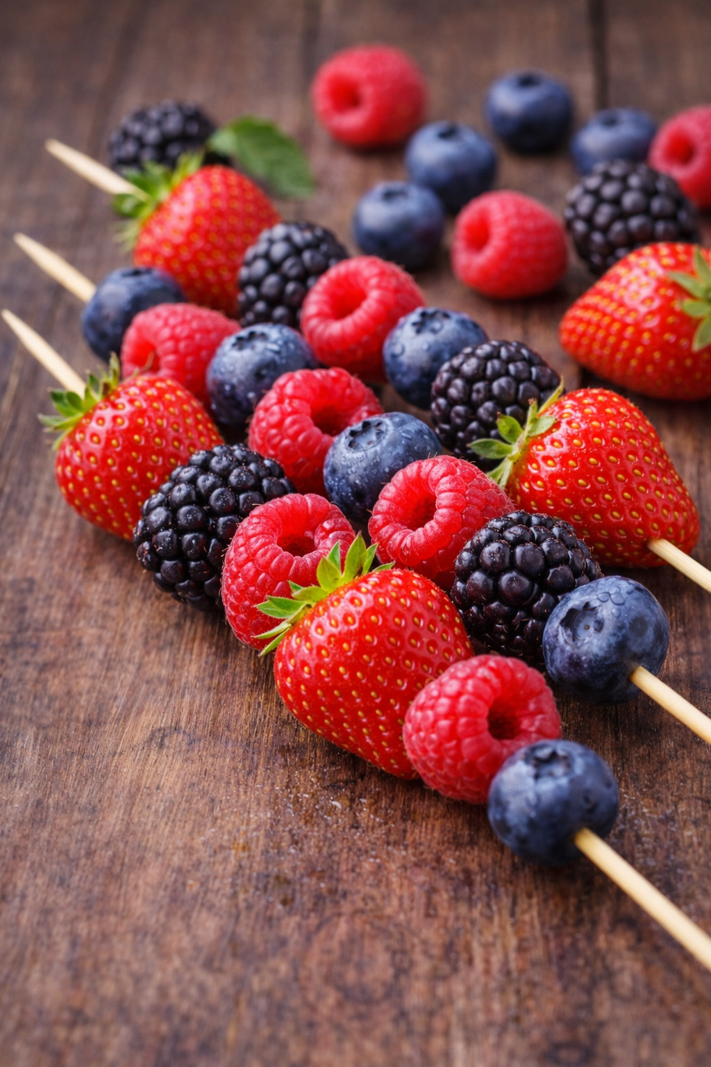 Basket of mixed berries including strawberries, blueberries, and raspberries on a wooden background.